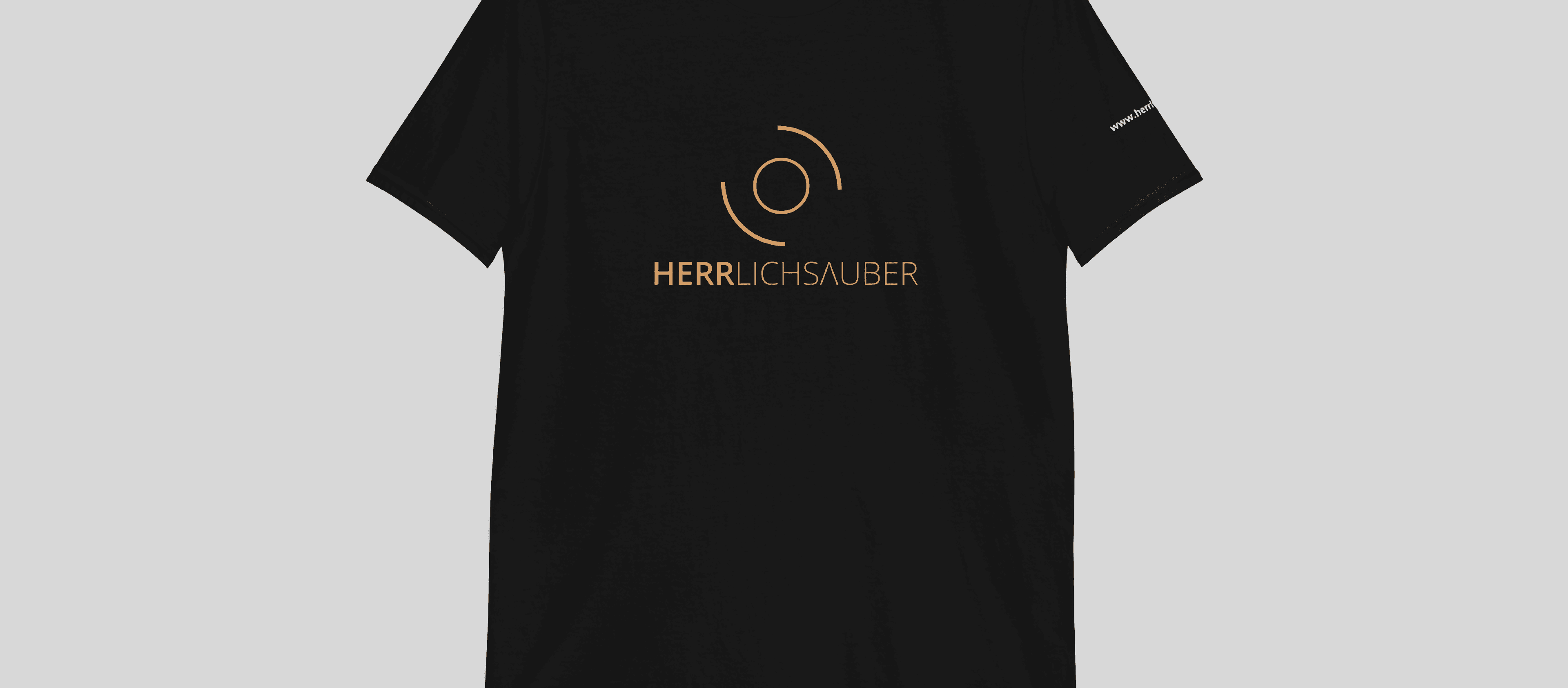 Schwarzes T-Shirt mit dem herrlichsauber-Logo in Kupfer vor grauem Hintergrund